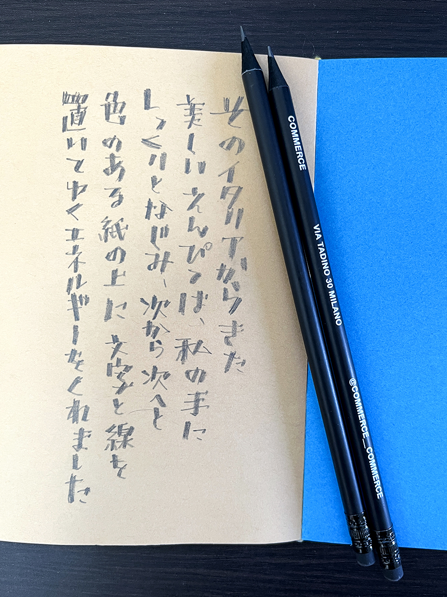 茶色い紙に鉛筆で書かれた日本語の縦書き文字と、2本の黒い鉛筆。イタリアの鉛筆で文字を描く喜びをテーマにしたカリグラフィー作品です。