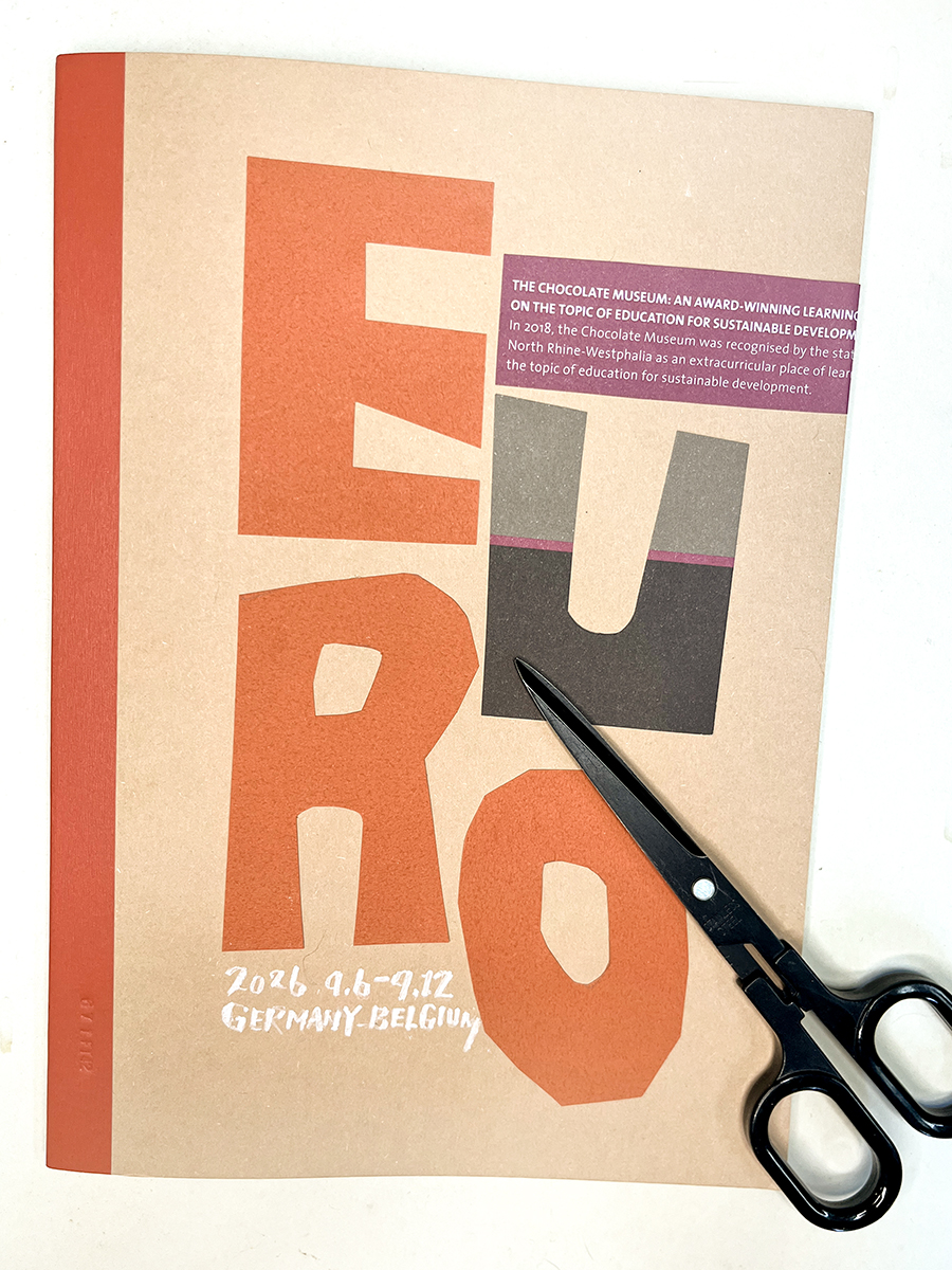 クラフト紙の表紙に貼った、切り抜きの「EURO」の文字と、横に置いた黒いハサミ。旅の記憶を振り返る時間をテーマにした、手作りの旅ノート作品。